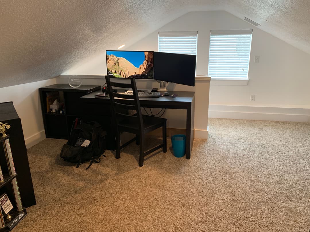 Cozy attic office with dual monitors, a desk, chair, and carpeted flooring.