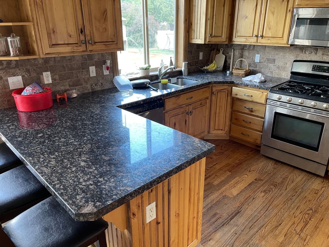Modern kitchen with granite countertops, wooden cabinets, stainless steel appliances, and bar seating.