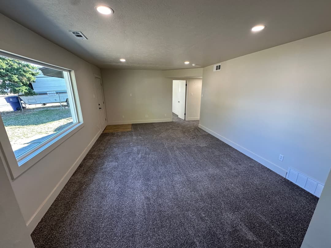 Spacious living room with large window and neutral carpet in modern home setting.