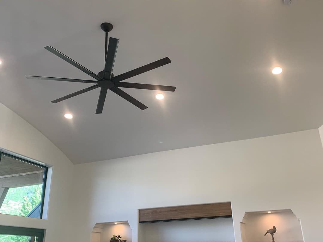 Ceiling fan with eight blades in modern living room with recessed lighting and white walls.