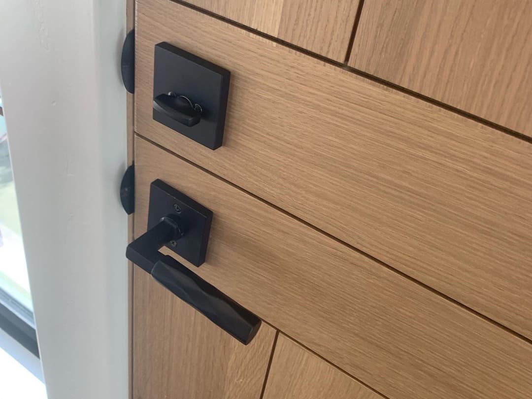 Modern wooden door with sleek black handle and lock hardware details.