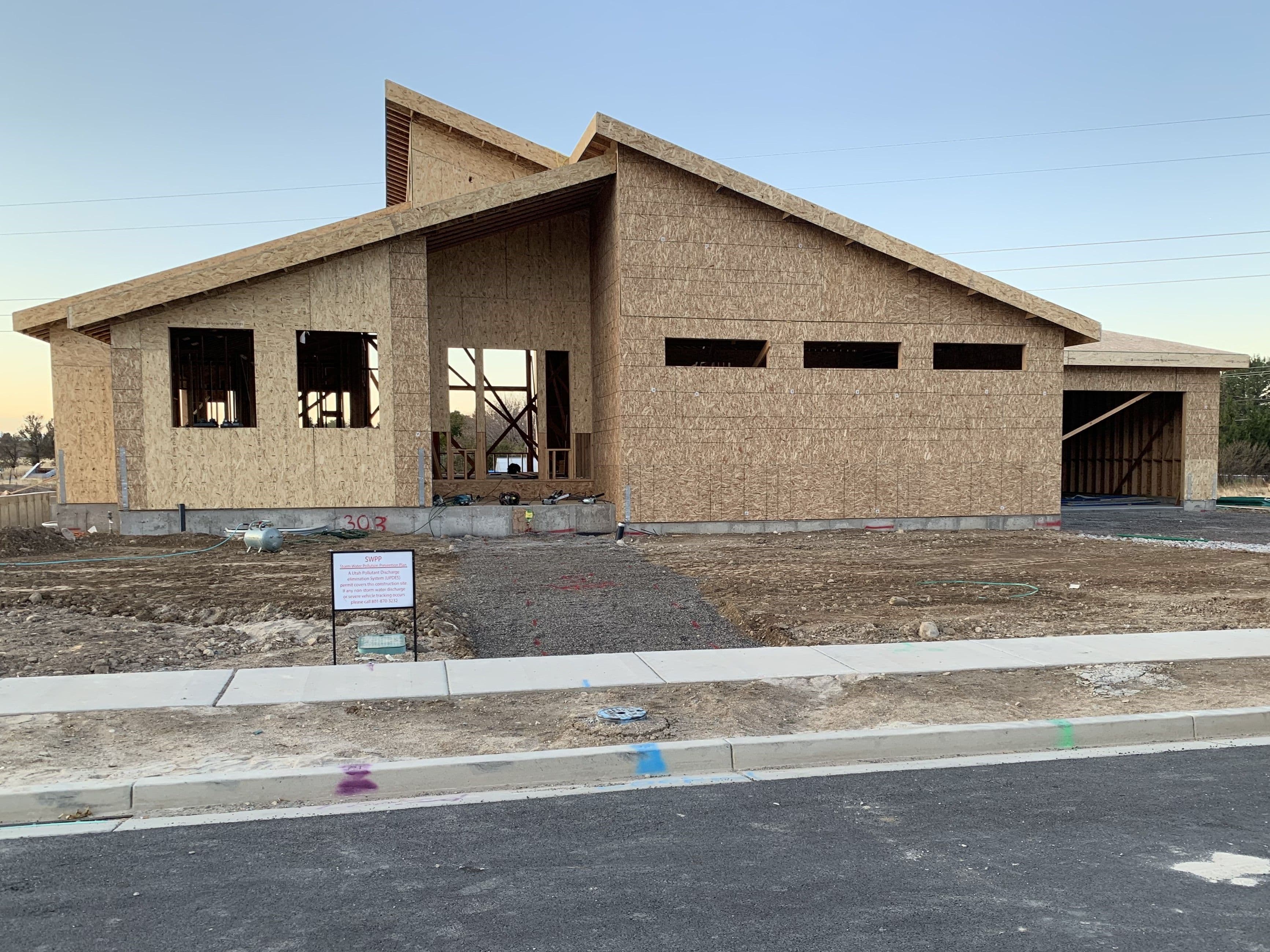 Construction of a modern house with exposed framing in a residential neighborhood.