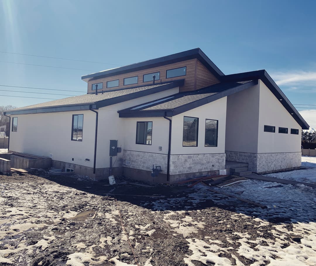 Modern two-story house with a mix of siding and stone exterior, snowy ground and clear blue sky.