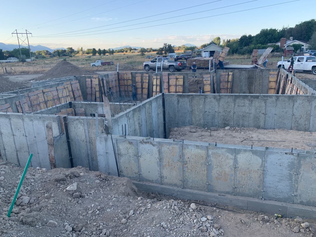 New concrete foundation construction site with wooden forms and machinery in rural landscape.