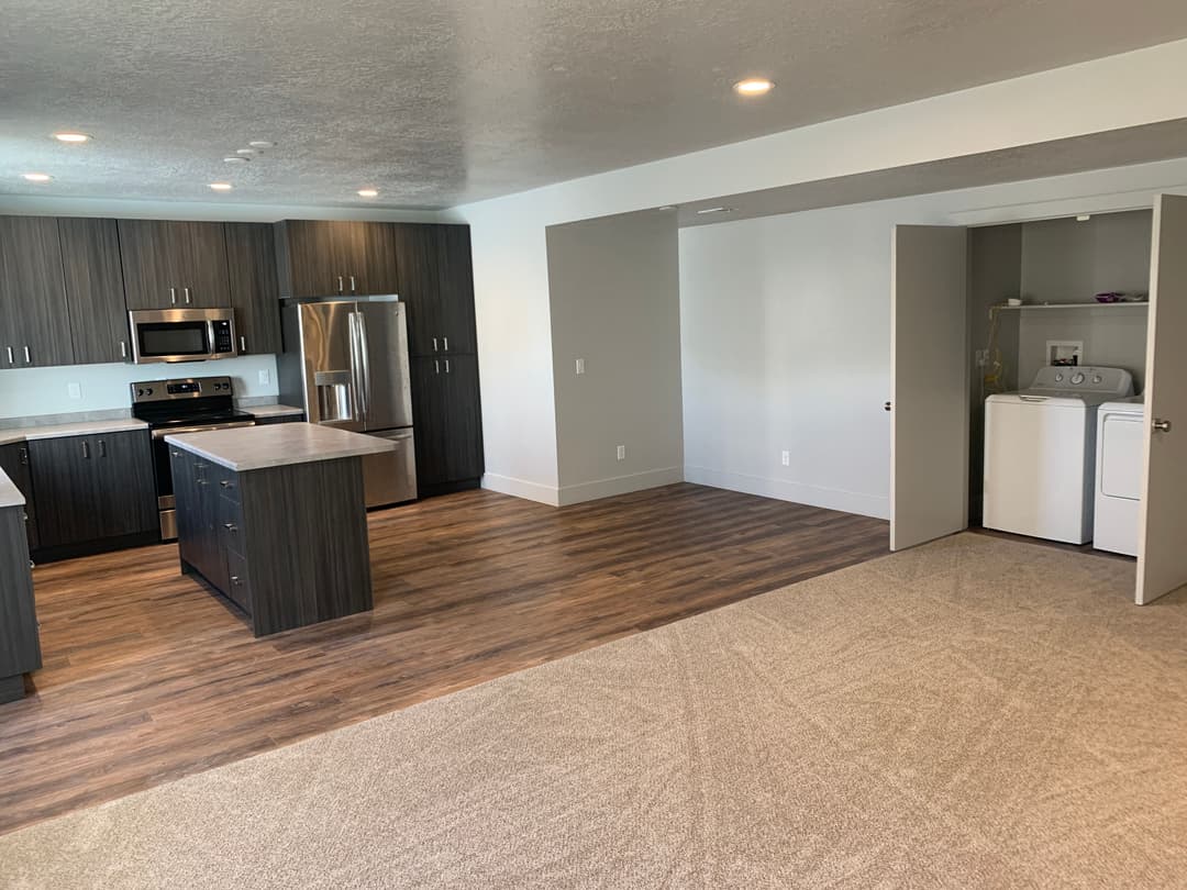 Modern kitchen and living area with dark cabinetry, stainless steel appliances, and laundry space.