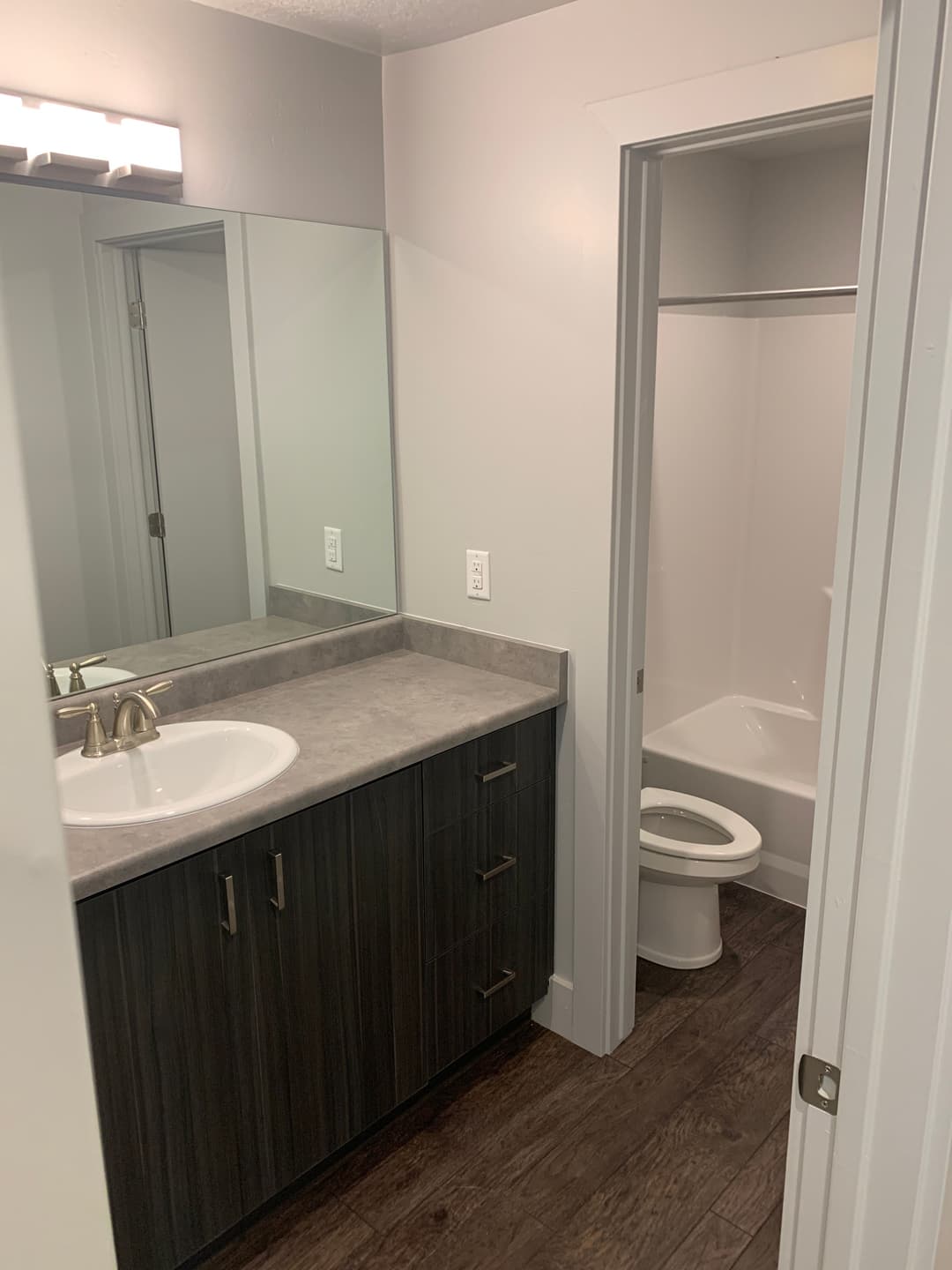 Modern bathroom with gray countertops, dark wood cabinetry, and separate shower area.
