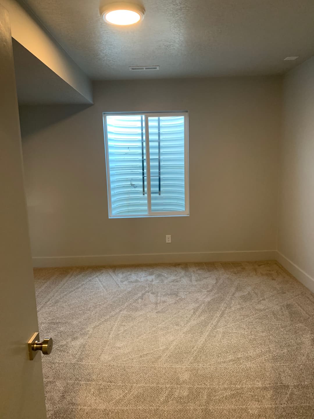 Empty room with beige carpet, a window with blinds, and modern lighting. Ideal for renovation.