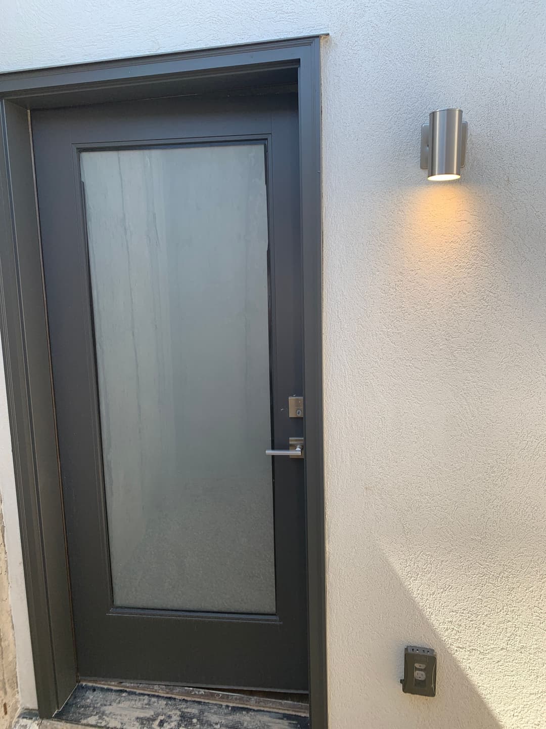 Modern gray entrance door with frosted glass, stylish wall light, and sleek doorbell button.