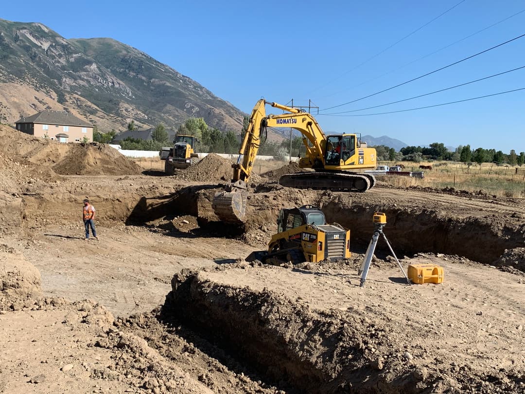 Construction site with heavy machinery excavating land, mountains in the background.