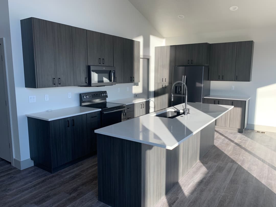 Modern kitchen with dark cabinetry, stainless steel appliances, and a large island.