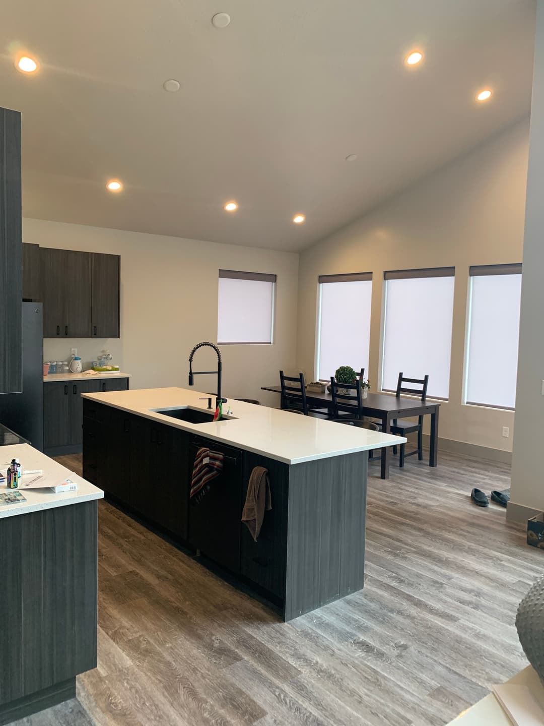 Modern kitchen with dark cabinets, white countertop, dining area, and natural light.