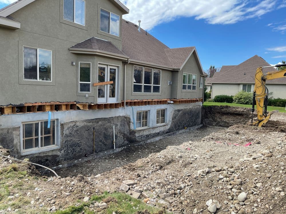 Home under construction with exposed foundation and excavation for basement expansion.